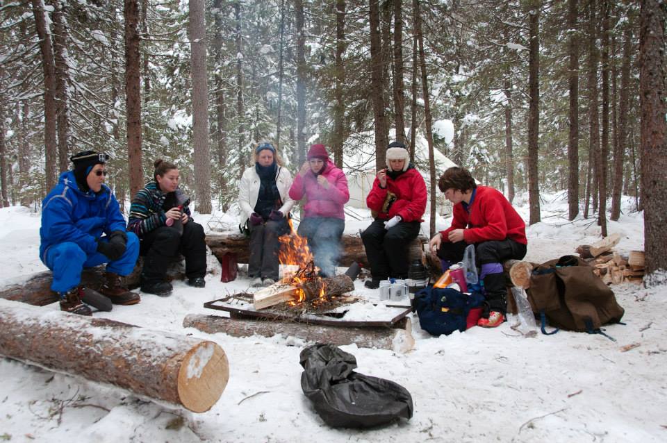 Bundled family sitting around a campfire in snowy woods