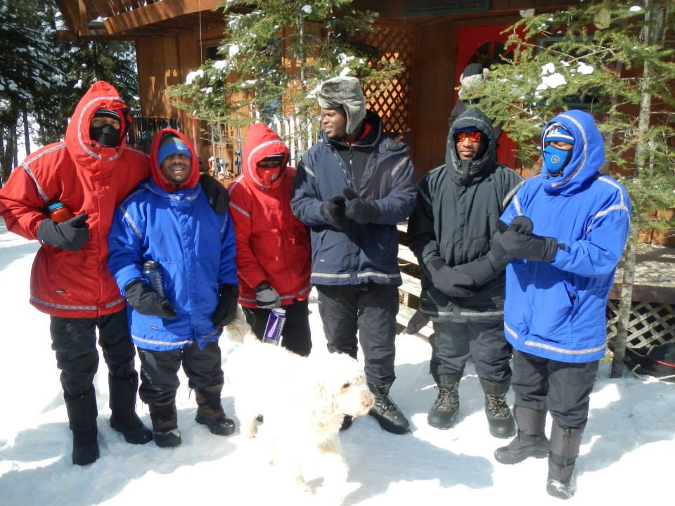 Six men in coordinated coats with a sled dog in the snow