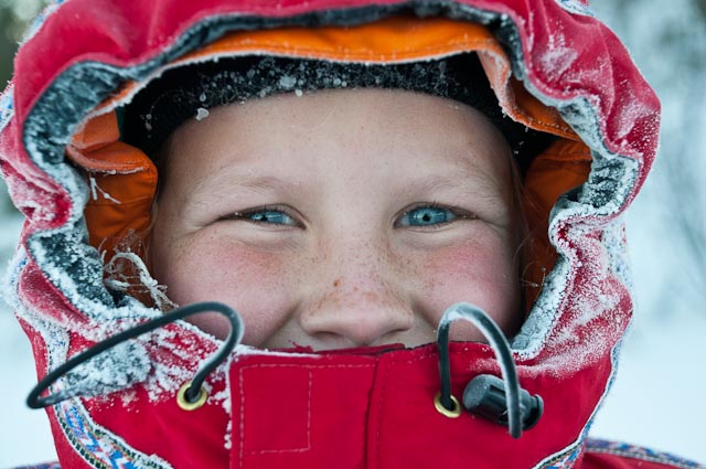 Kid smiling in the snow as winter coat covers their face