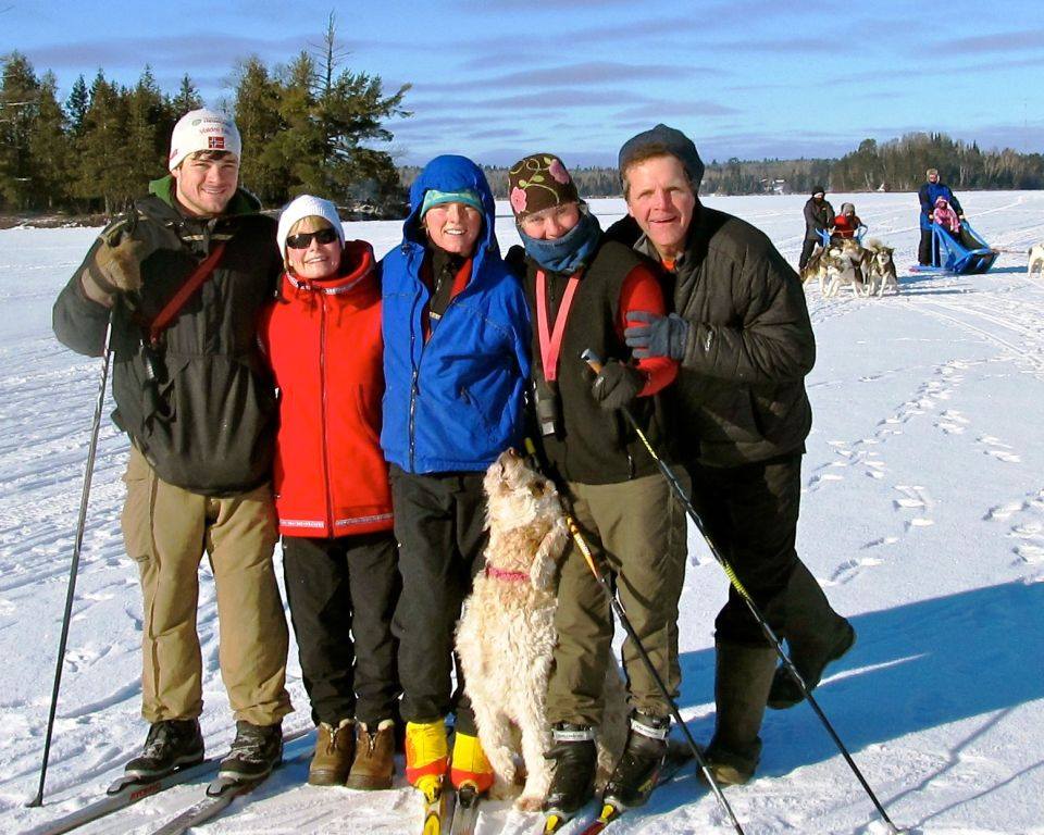 Family skiing with sled dogs in background