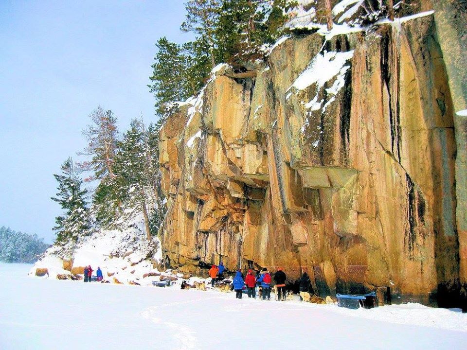 Large snowy cliff face with group of people standing beneath