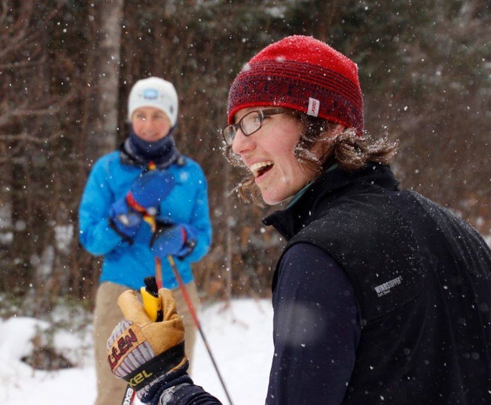 Man in glasses in the show with woman skiing in background