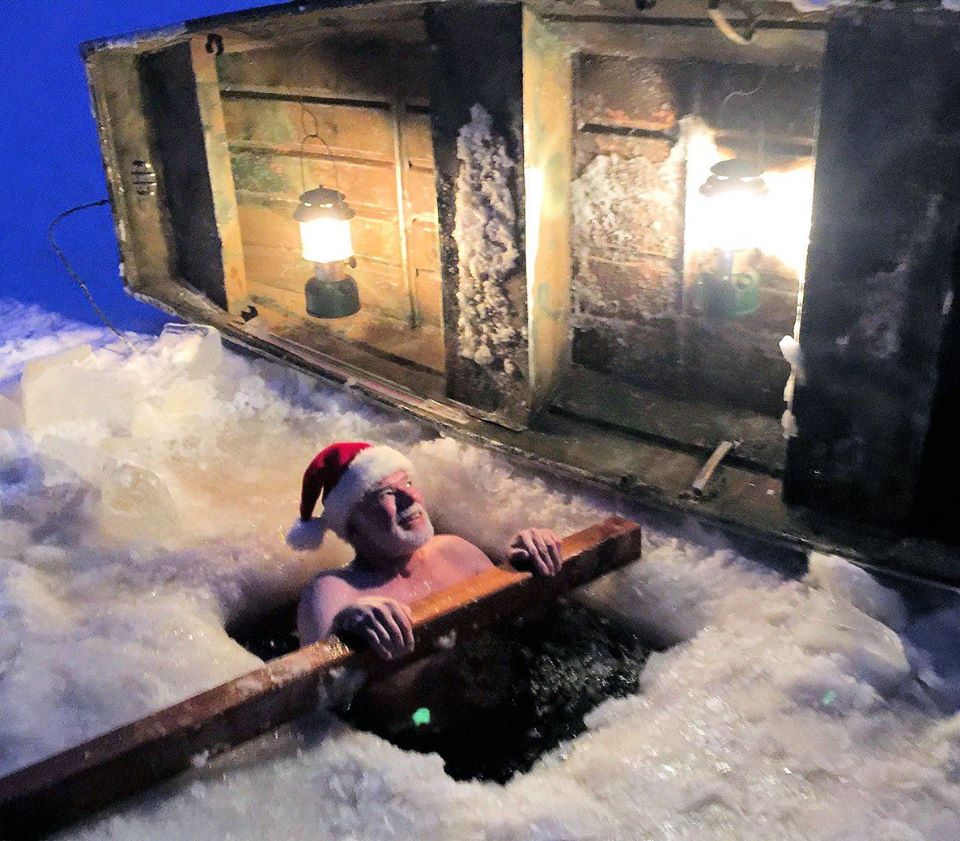 Man in santa hat takes a dip in a frozen lake