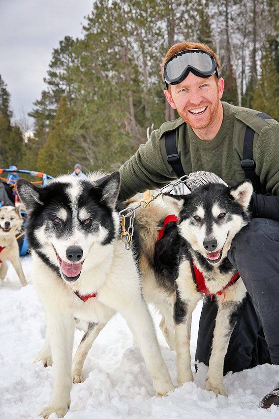 Man with goggles poses holding two sled dogs