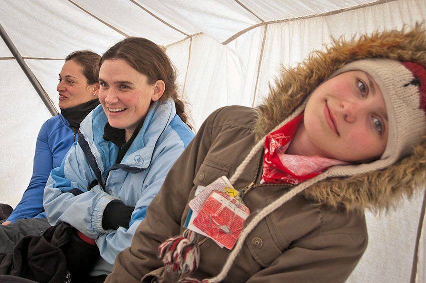 Three women in a tent, bundled up in coats smiling