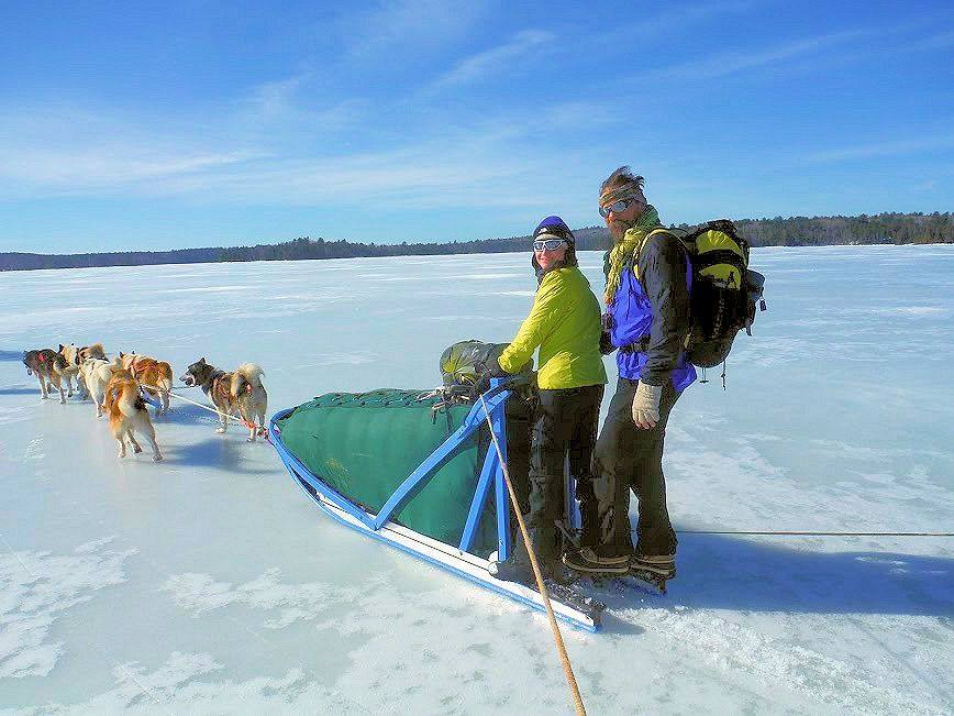 Couple on green sled with six dogs smiling on frozen lake