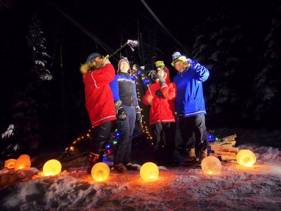 Four people celebrating new years on a snowy night with orange round lights at their feet
