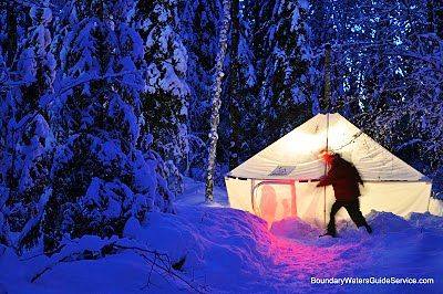 Man outside of a lit tent on a dark and snowy night