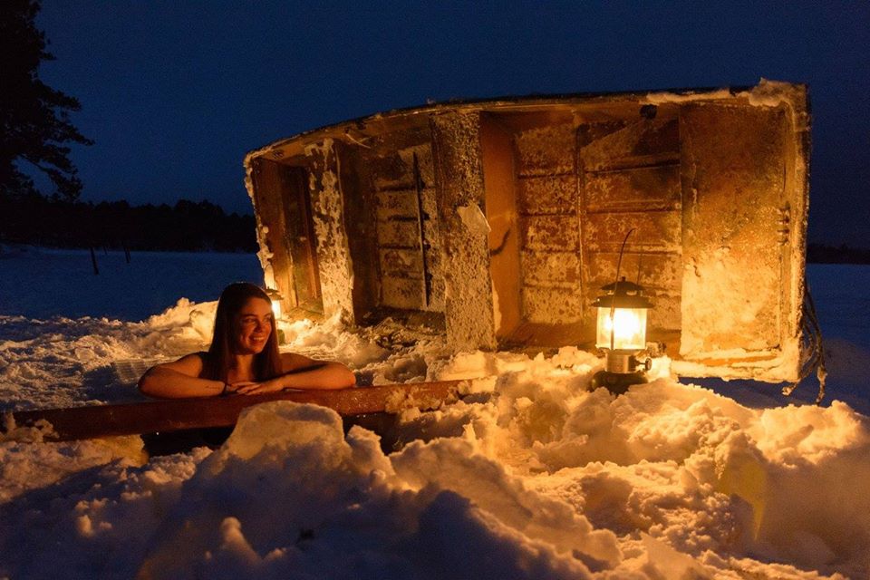 Woman alone in frozen lake bath at night with a warm lantern light