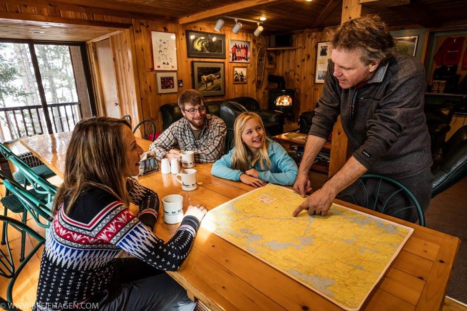 Four people in a cabin using a map to plan their sledding route