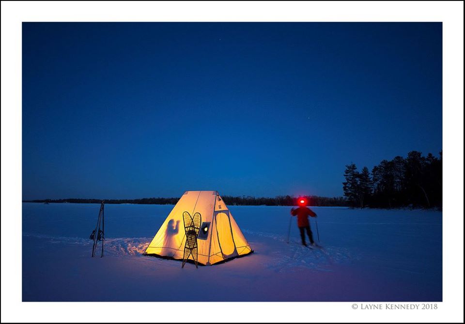 Small lit tent on frozen lake with a skiier outside
