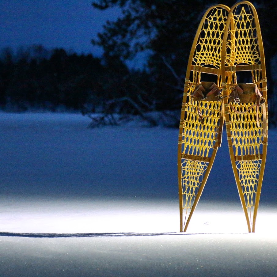 Large teardrop netted snowshoes stick out of freshly dropped snow at night