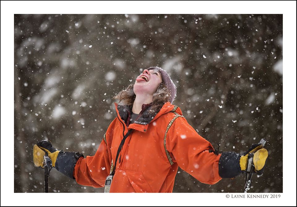 Teen looking up at snow with their arms open and tongue out