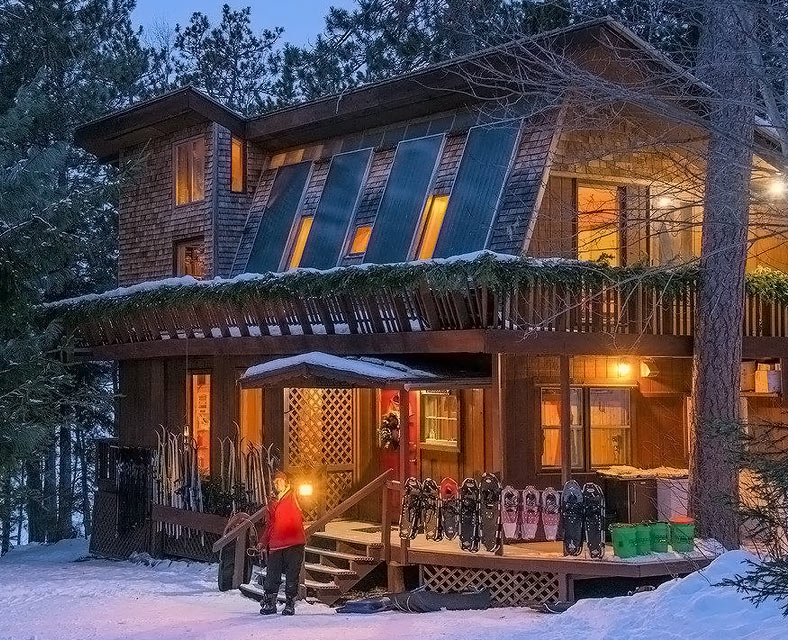 Man standing with a lantern outside a snowy wooden house